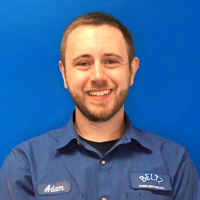Meet The Team | Beltz Home Service Co. A Smiling Man In A Blue Work Shirt, Proudly Wearing &Quot;Adam&Quot; And &Quot;Beltz Home Service Co.&Quot; Patches, Stands Against A Bright Blue Background. He'S A Vital Part Of The Dedicated Team That Ensures Quality Service Every Day.