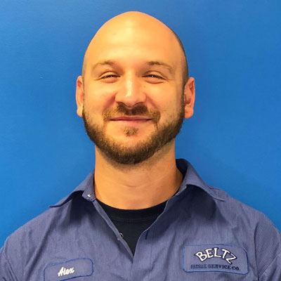 Meet The Team | Beltz Home Service Co. A Person In A Blue Uniform Shirt Stands Against A Vibrant Blue Background, Smiling Like A Proud Team Member. &Quot;Beltz&Quot; Is Embroidered On The Shirt.