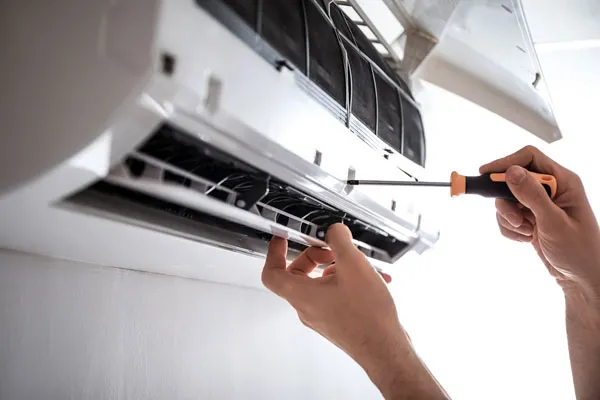 A person uses a screwdriver to skillfully maintain a wall-mounted air conditioning unit, ensuring optimal performance in this mini-split installation.