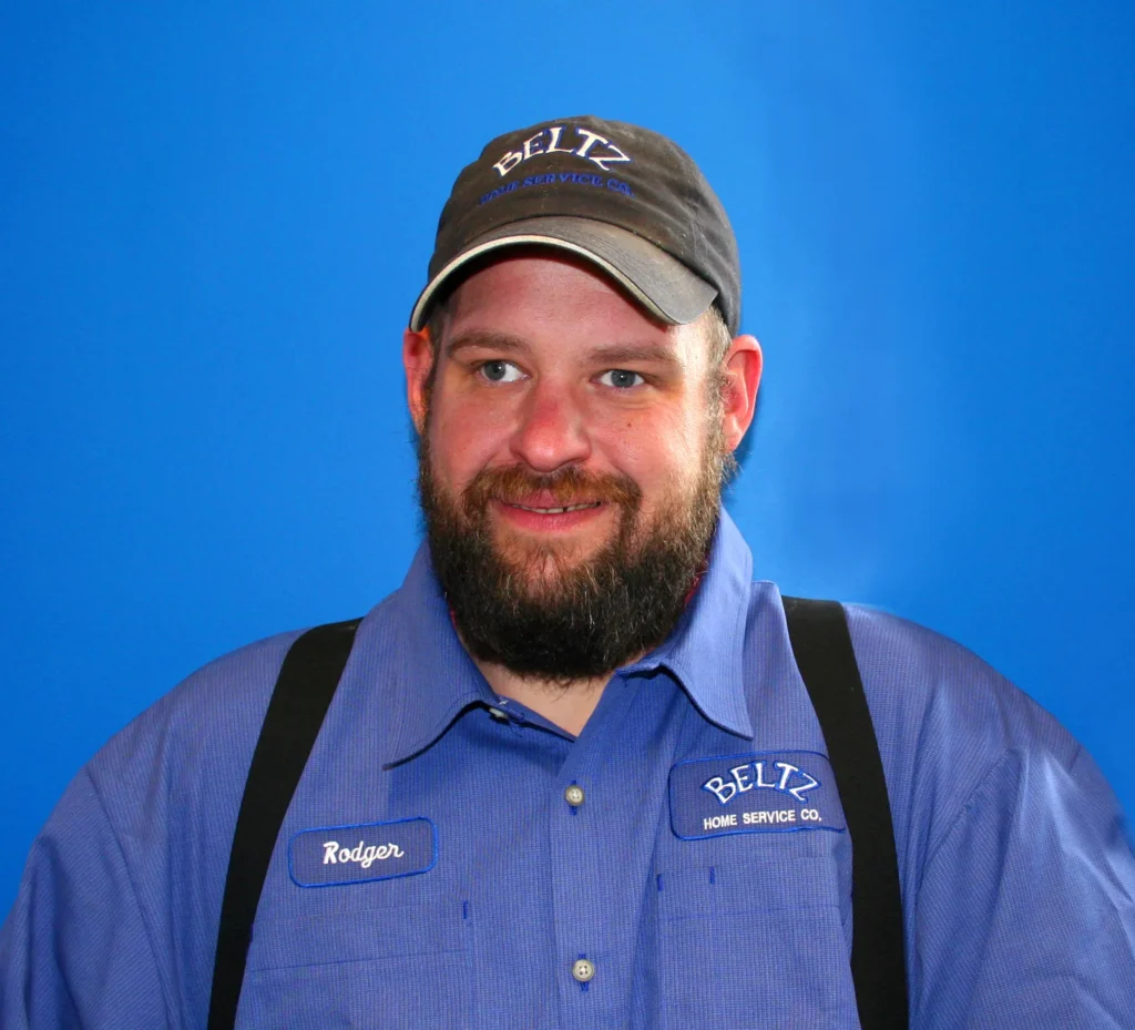 Meet The Team | Beltz Home Service Co. A Man In A Blue &Quot;Beltz Home Service Co.&Quot; Uniform And Cap, Representing The Team, Stands In Front Of A Solid Blue Background. He Has A Beard And Is Smiling Slightly.