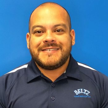 Andy-Walles A Bearded Member Of The Team Smiles At The Camera, Wearing A Navy Blue Polo Shirt With The &Quot;Beltz Home Service Co.&Quot; Logo. The Background Is Solid Blue.