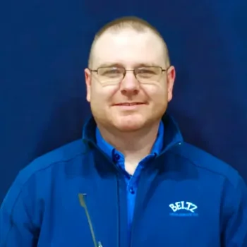 Benjamin-1 A Man Wearing Glasses, A Blue Zipped Jacket With The &Quot;Beltz&Quot; Logo, And A Blue Shirt Stands Confidently Against A Dark Blue Background, Looking Towards The Camera With A Sense Of Team Spirit In His Gaze.